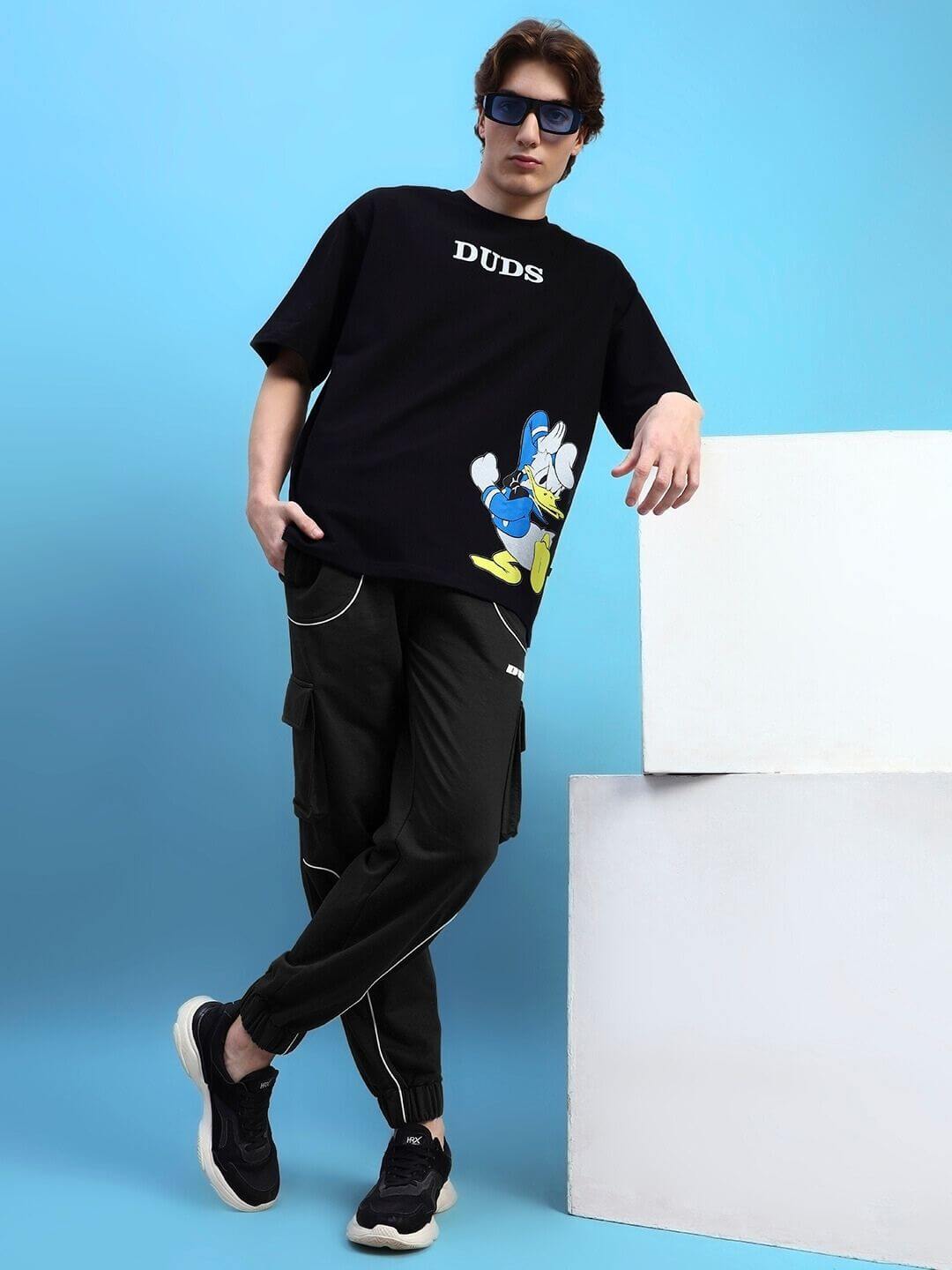 Model wearing DEVENO relaxed-fit joggers in black with DUDS logo, showcasing comfortable fashion style.
