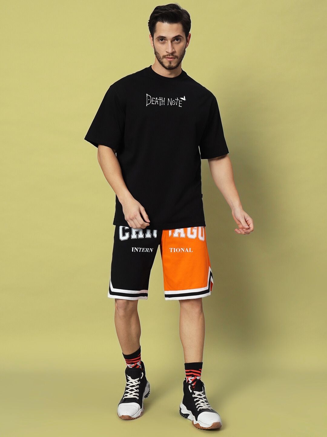 Man wearing FOLLOW LIFE OVERSIZED T-SHIRT BLACK with colorful shorts, standing against a light background.