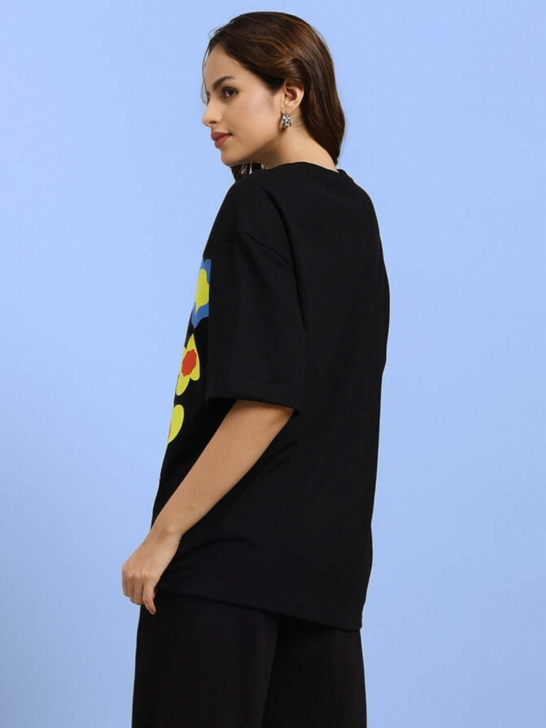Woman wearing black oversized Hollister t-shirt, side view, featuring colorful graphic design. Premium cotton blend, casual style.