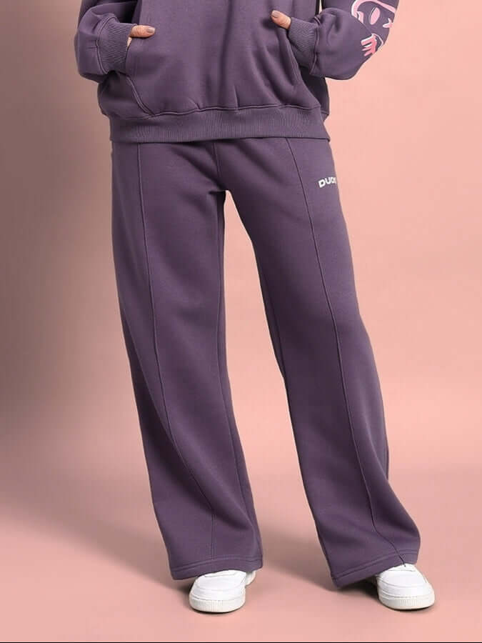 Woman wearing violet Casper fleece jogger pants with white sneakers, casual outfit against a pink background.