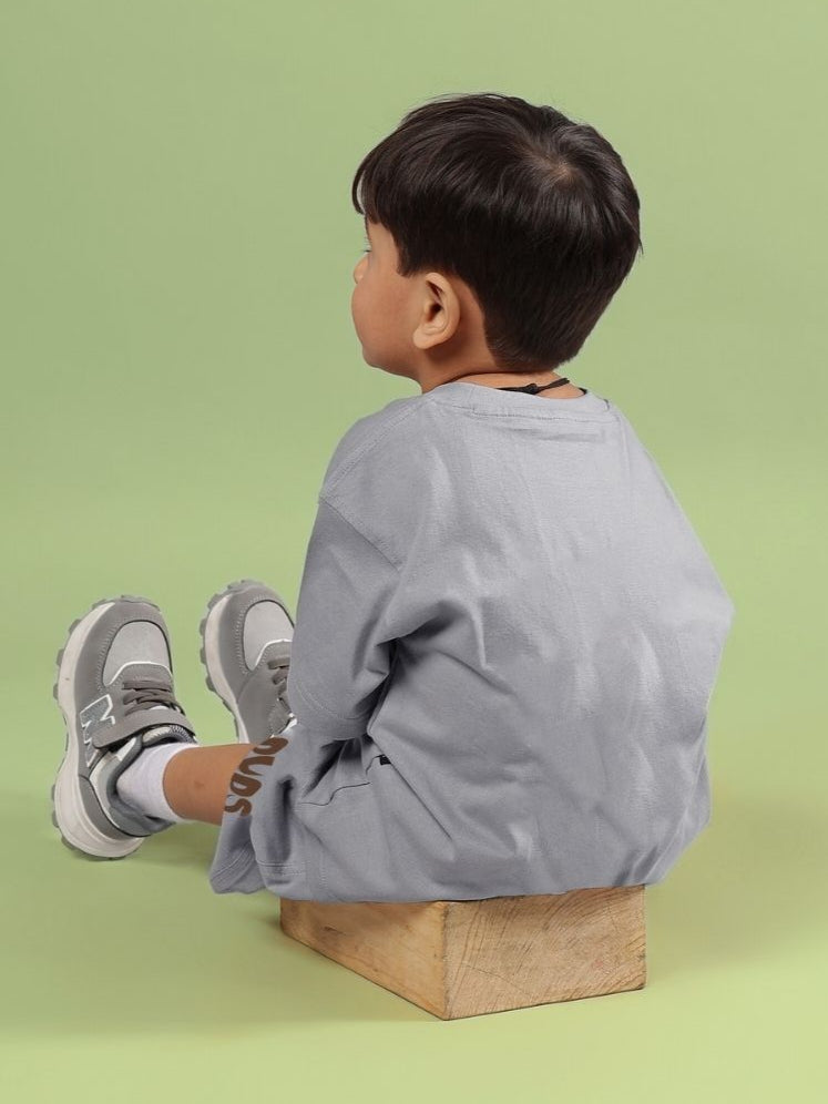Child wearing a Flint Bunny grey t-shirt, seated on a wooden block, showcasing unisex design for boys and girls.