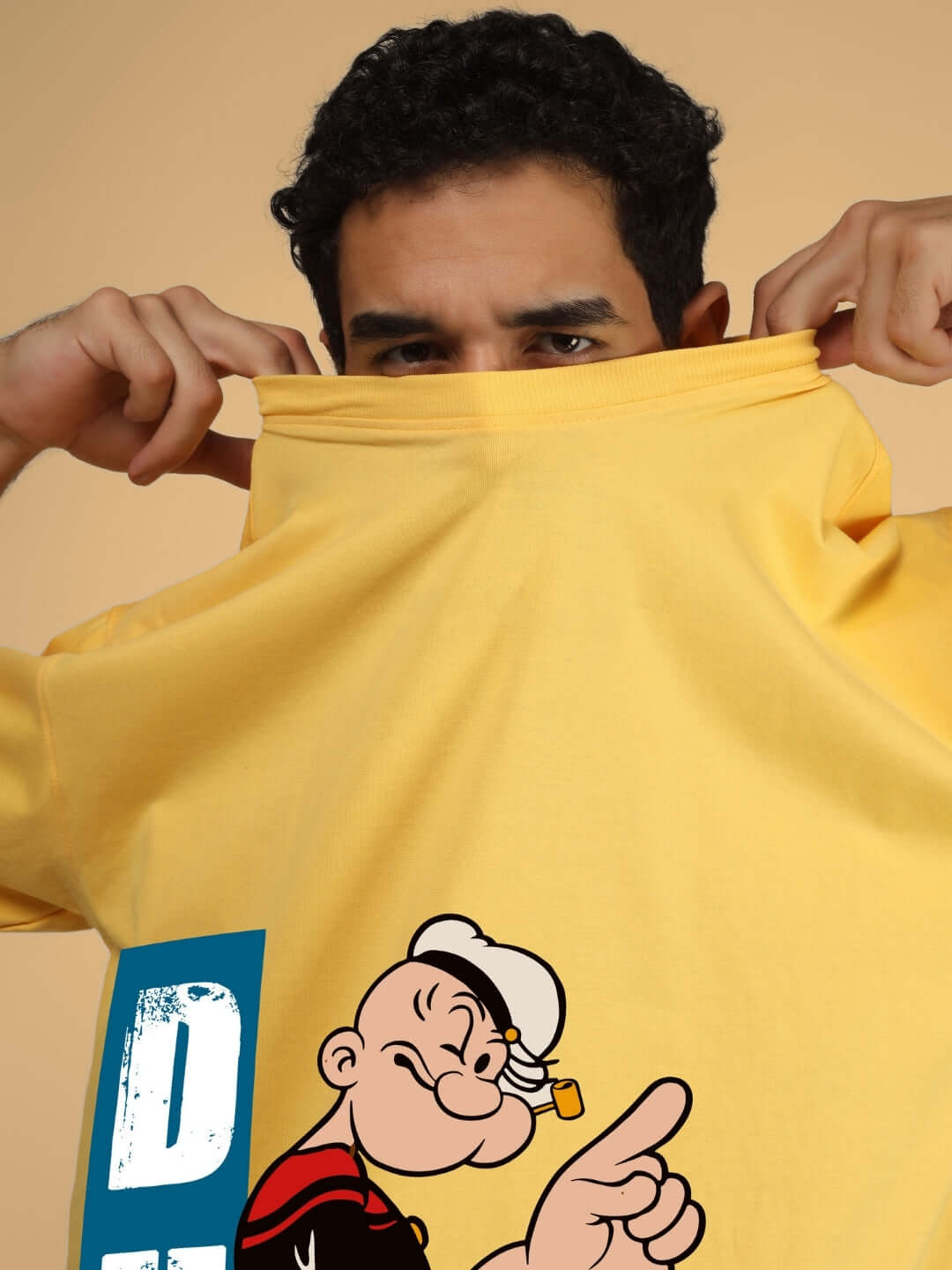 Model wearing POPEYE OVER-SIZED T-SHIRT YELLOW with cartoon graphic, showcasing custom fit option on DUDS for personalized sizes.