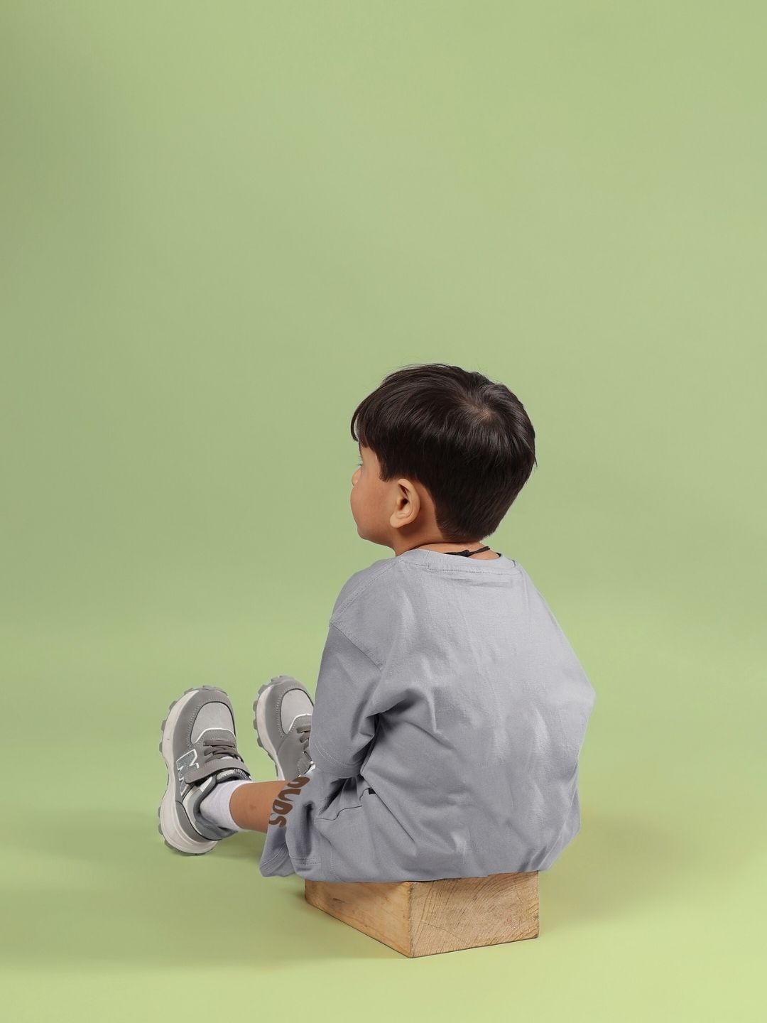 Child wearing Flint Bunny co-ord set in grey sitting on a wooden box against a green background, showcasing a stylish unisex outfit for boys and girls.