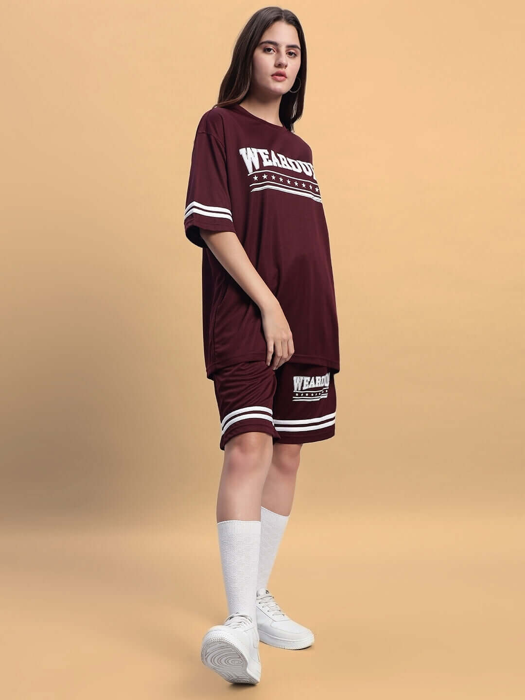 Woman wearing wine colorblock co-ord set, sports style with white socks and sneakers, styled for casual wear against beige background.
