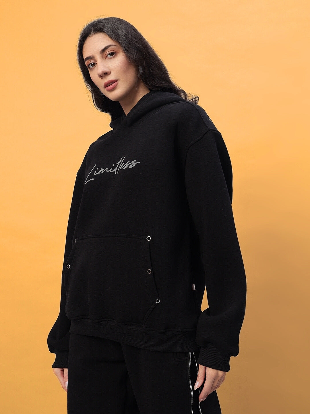 Woman wearing a black fleece co-ord with 'Limitless' design, featuring reflective details, against a mustard background.