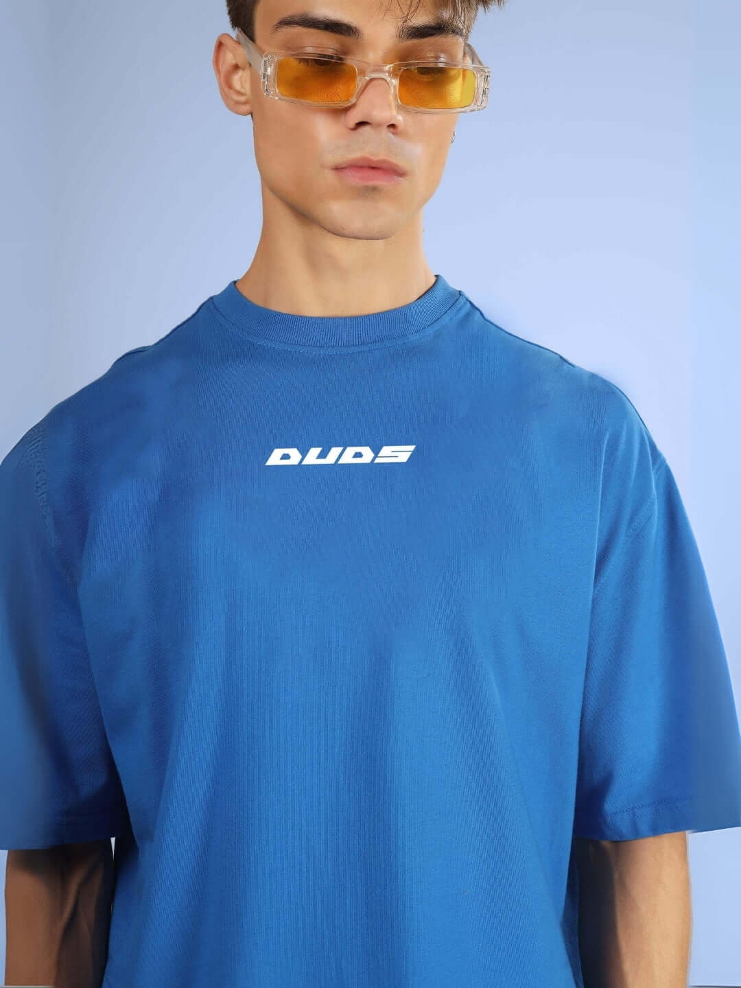 Model wearing DUDS VAN OVER-SIZED T-SHIRT ROYAL BLUE with logo, showcasing casual fashion in vibrant blue, perfect for a trendy look.
