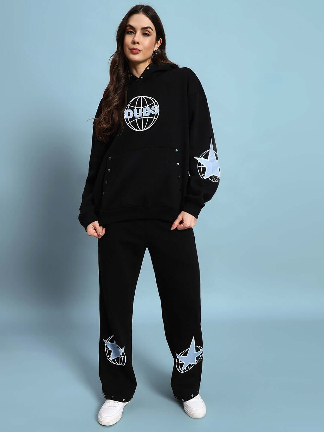 Woman wearing black fleece jogger set with global star design, standing against a blue background.