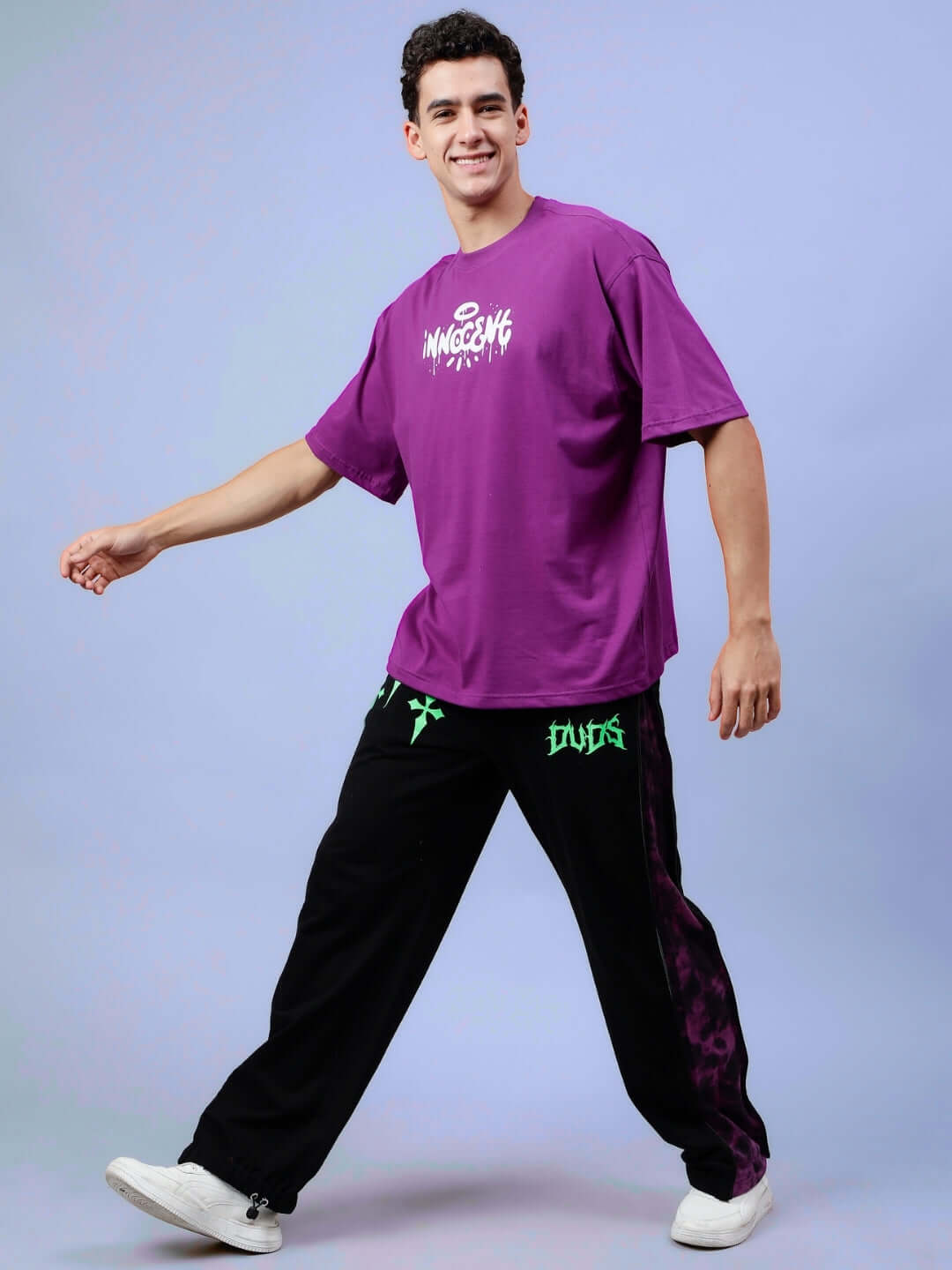 Person wearing INNOCENT OVER-SIZED T-SHIRT PURPLE and black pants, casually walking.