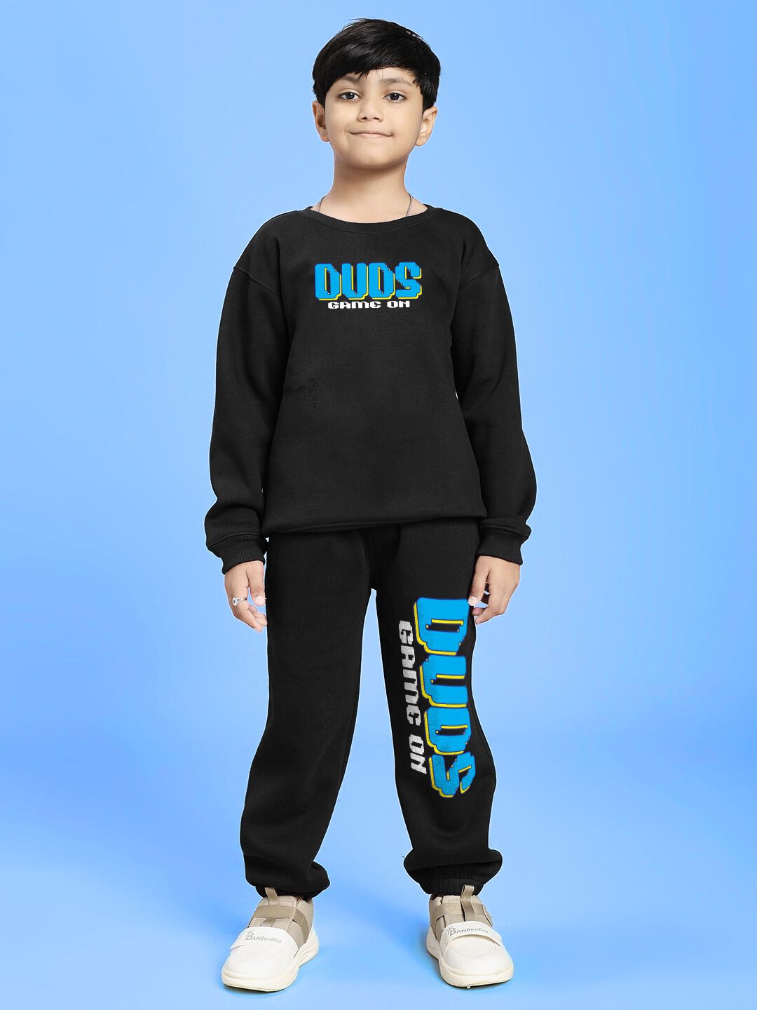 Child wearing GAME ON PRINT FLEECE JOGGER FOR BOYS AND GIRLS BLACK against blue background.