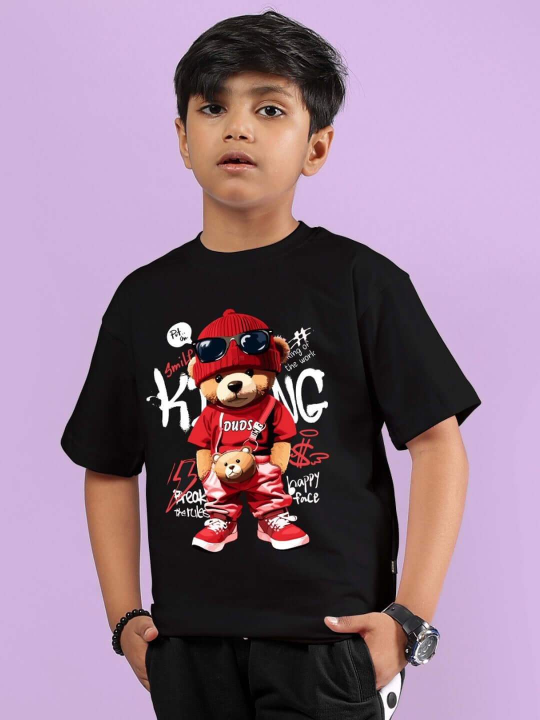 Boy wearing black hip hop teddy t-shirt with colorful graphics, hands in pockets, against a lavender background.