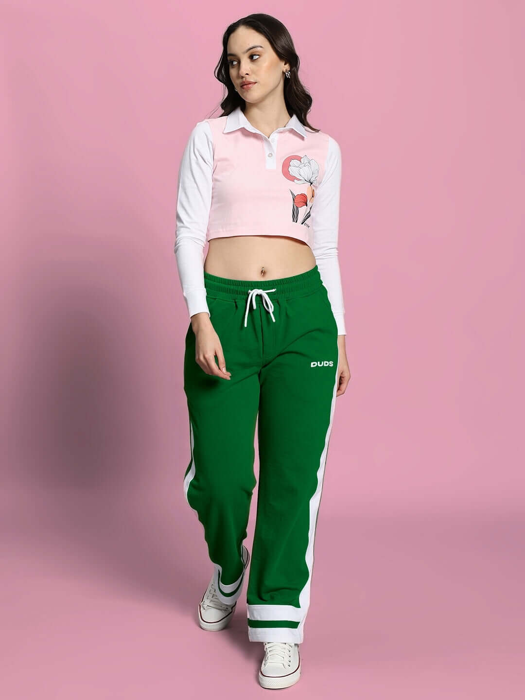 Model wearing green women's Ronny side stripe jogger by DUDS, walking confidently on a pink backdrop.