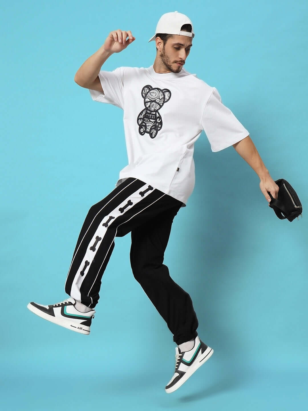 Alt Tag: Model wearing Tibia Contrast Panel Joggers Black with graphic tee and sneakers against blue background