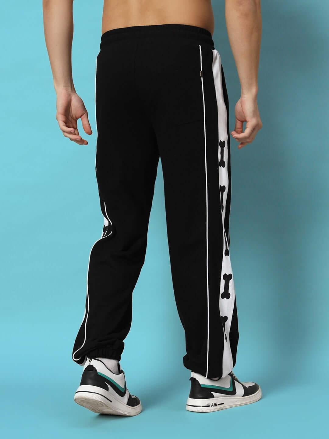 Back view of TIBIA CONTRAST PANEL JOGGERS BLACK with white side panels and bone print detail, worn by a model against a light blue background.