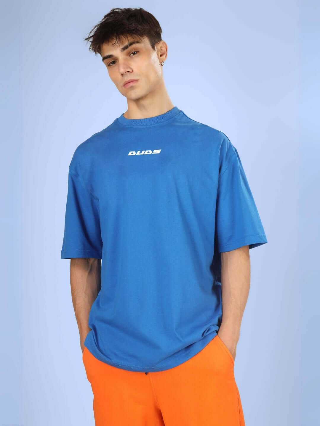 Model wearing LUCKYSTAR OVER-SIZED T-SHIRT ROYAL BLUE with orange pants, showcasing casual streetwear style.