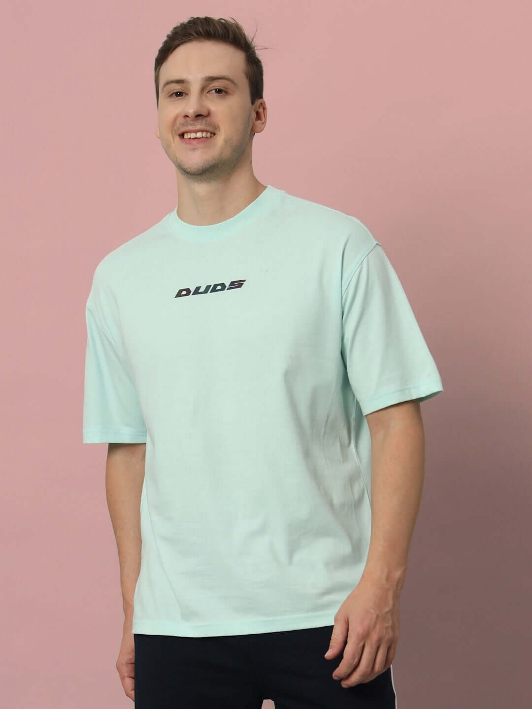 Man wearing LIVE GENTY UPON THIS EARTH OVER-SIZED T-SHIRT SKY BLUE against pink background