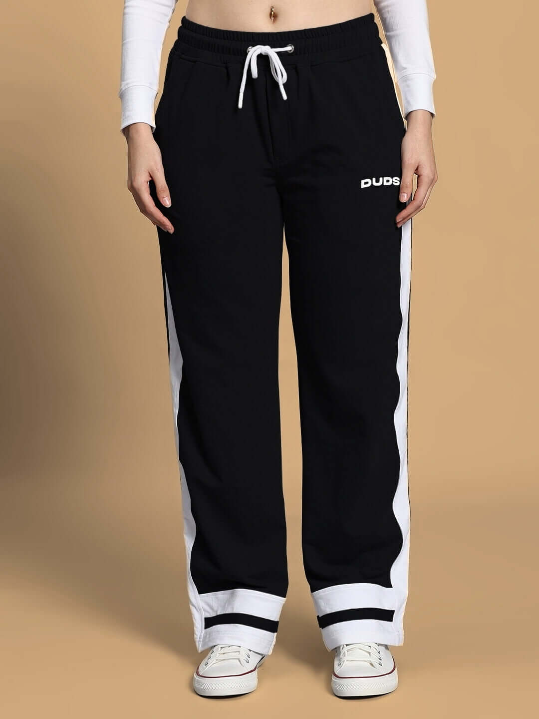 Person wearing black jogger pants with white stripes and logo, paired with white sneakers, against a neutral background.