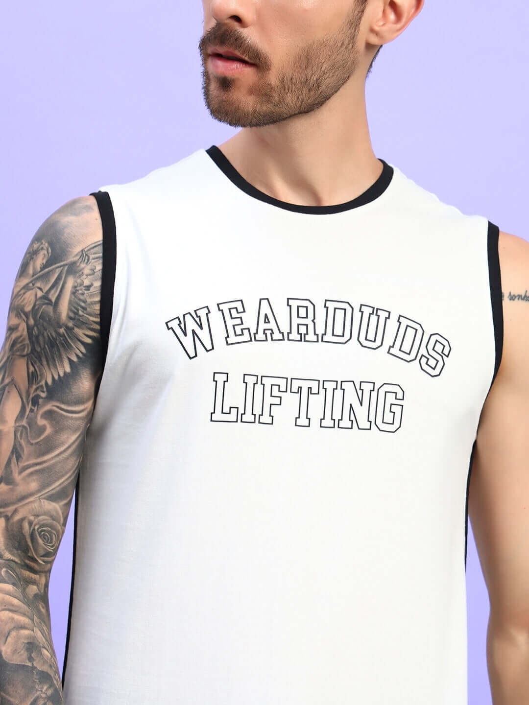 Man wearing a sleeveless white t-shirt with 'Wearduds Lifting' text and tattooed arm, standing against a purple background.