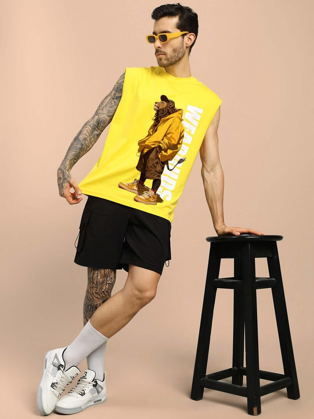 Male model wearing a yellow STREET LION GYM T-shirt with a lion graphic, paired with black shorts and sneakers, against a beige background.