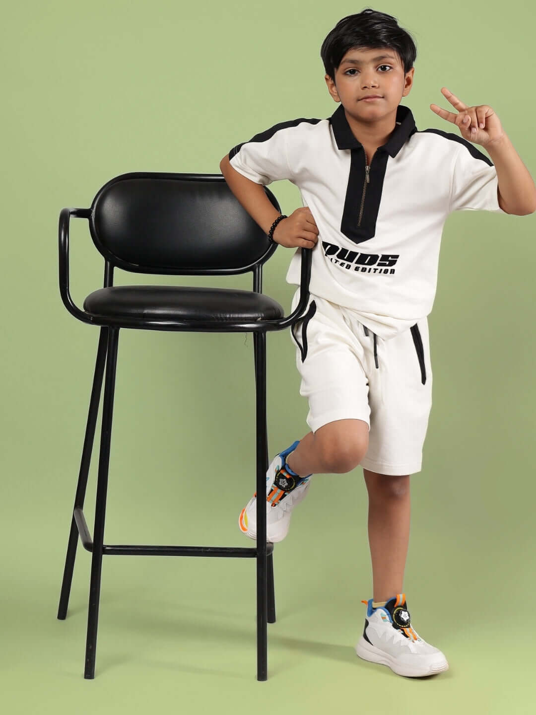 Child wearing an off-white Splinter t-shirt by DUDS, standing next to a chair, showcasing kids' casual fashion for boys and girls.