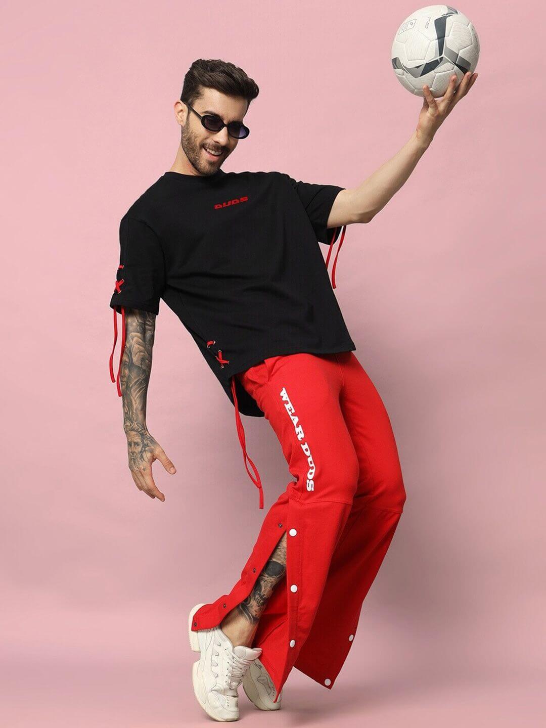 Man wearing a black oversized t-shirt made of premium cotton French terry, styled with red pants, posing with a soccer ball against a pink background.
