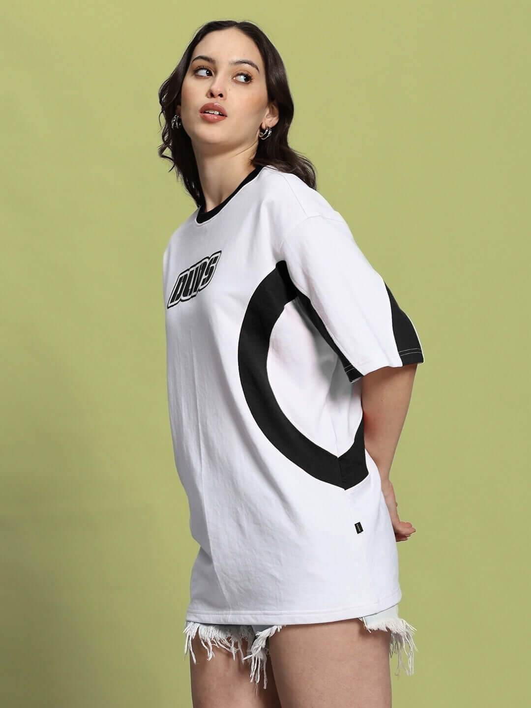 Woman wearing a white-black oversized T-shirt with bold print and denim shorts, standing against a light green background.