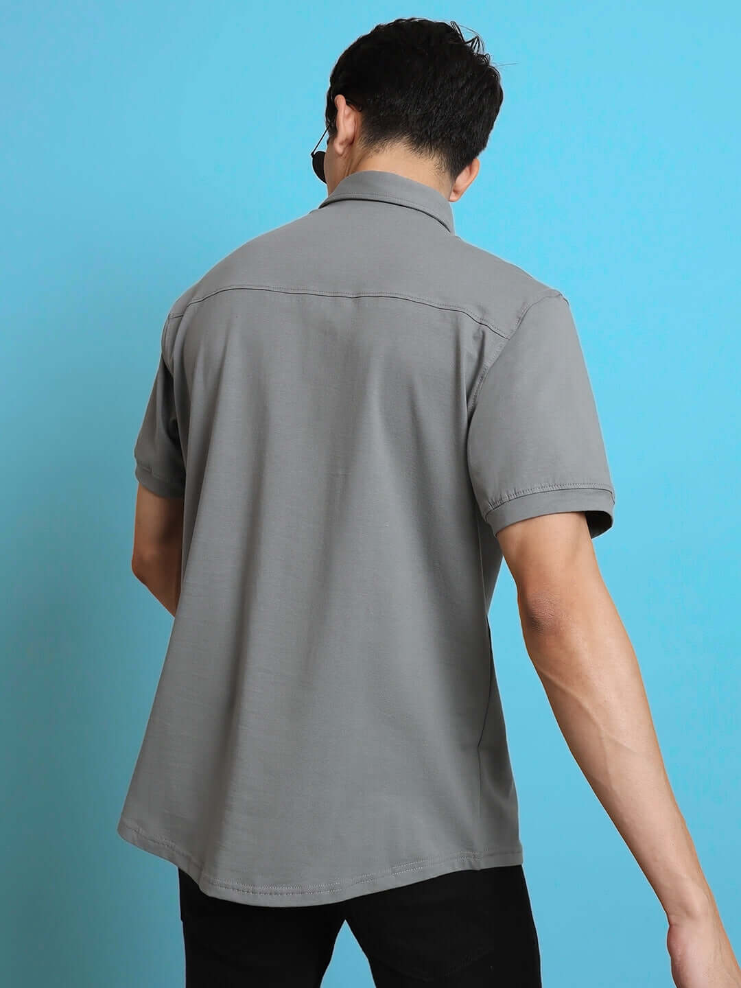 Back view of a model wearing a noir grained wrinkle-free shirt with curved hem and half sleeves. Made from 100% cotton lycra.