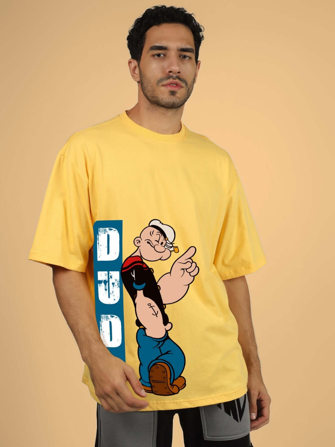 Man wearing POPEYE OVER-SIZED T-SHIRT YELLOW with cartoon print and DUDS logo.
