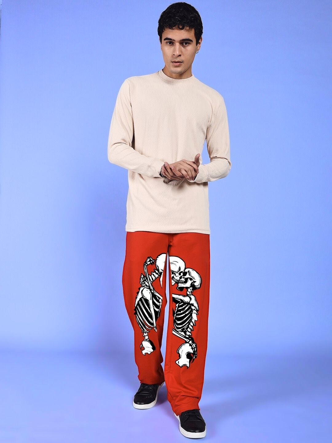 Model wearing SKELETONS LOVE RELAXED FIT JOGGER RED with skeleton graphic, standing against a blue background.