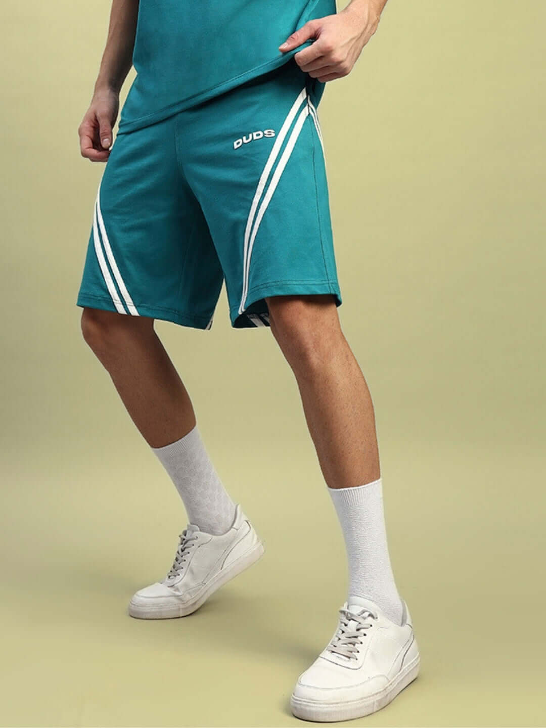 Man wearing STAR JUMPER regular fit teal shorts displaying stylish design, paired with white socks and sneakers, ideal for casual wear.