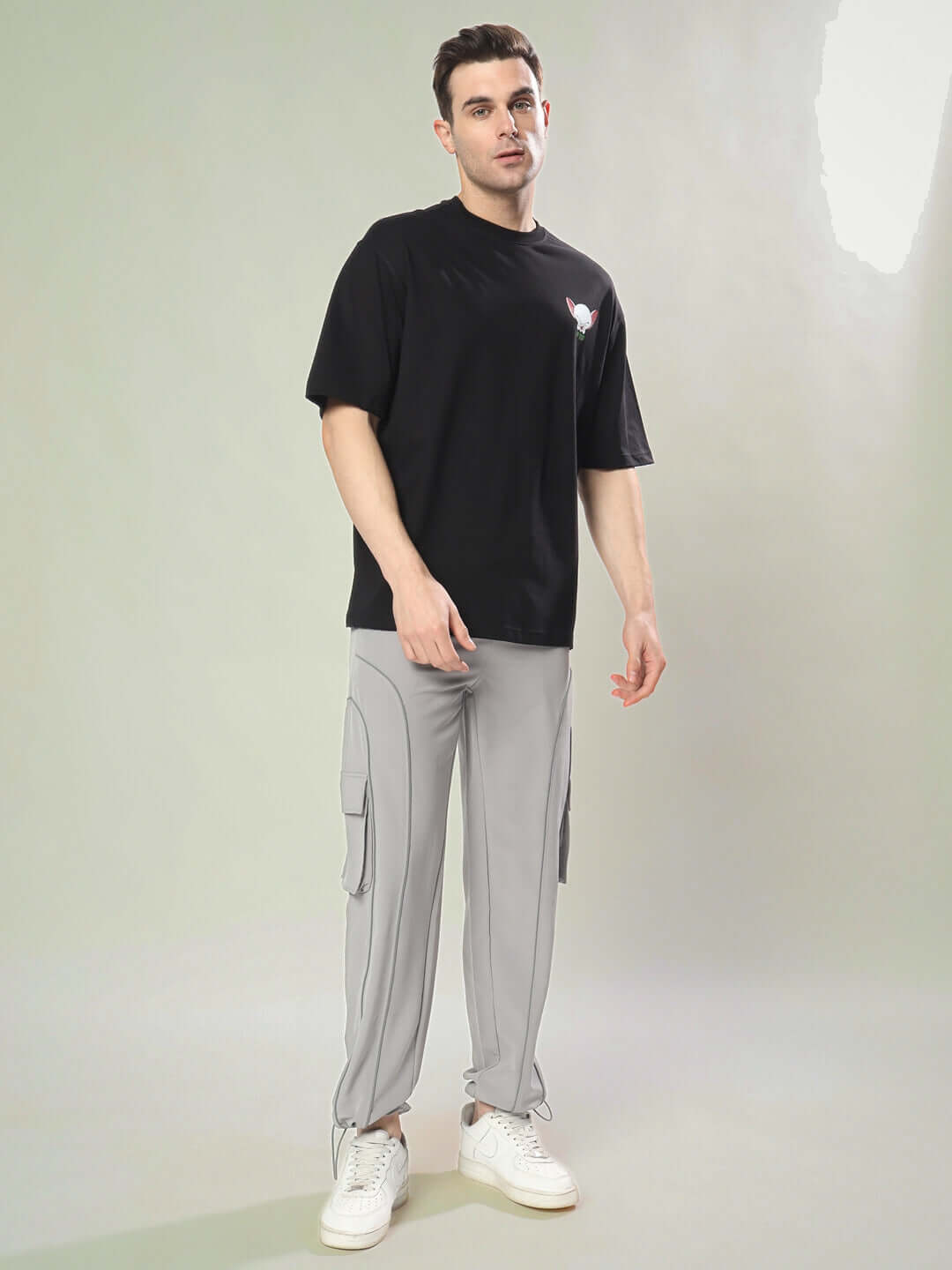Model wearing INSANE BRAIN OVER-SIZED T-SHIRT BLACK showcasing casual style with gray pants and white sneakers.