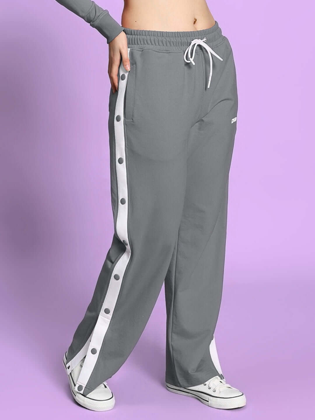 Grey women's relaxed fit jogger with white side buttons, worn by a model on a purple background, showcasing comfortable activewear.