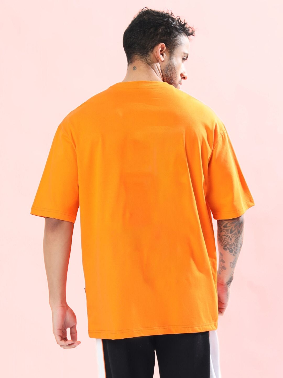 Back view of TOM AND JERRY TOAST OVERSIZED T-SHIRT ORANGE worn by a man, displayed on a pink background.