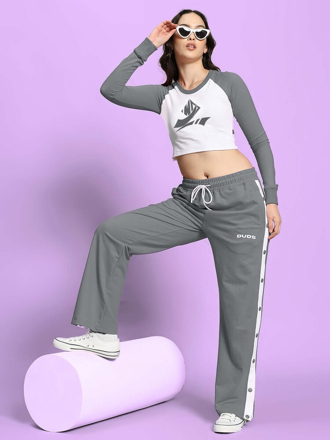Woman wearing grey relaxed fit jogger pants with side stripes, posing stylishly on a purple background.