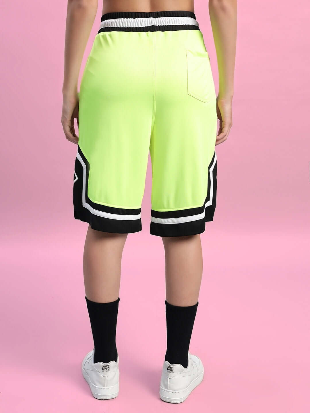 Back view of women's neon green Armado regular fit shorts, featuring a pocket and black accents, worn with black socks and white shoes.