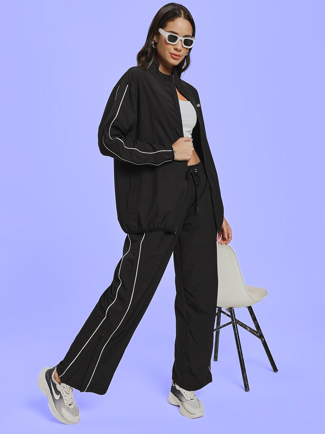 Woman wearing WOMEN RELIGHT RELAXED FIT CO-ORD SET BLACK with sunglasses, standing stylishly beside a chair on a light background.