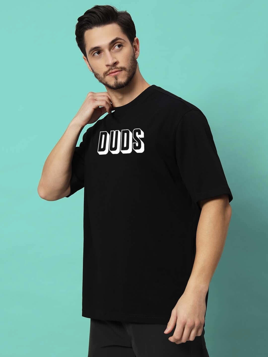 Man wearing DUDS PANTHER OVER-SIZED T-SHIRT BLACK against a teal background, showcasing front view with logo.