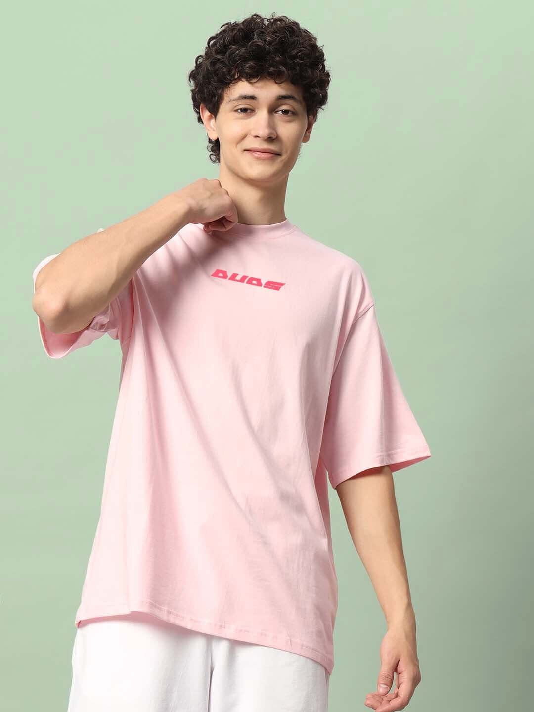 Alt Tag: Person wearing ILLUSION OVER-SIZED T-SHIRT PINK with text "DUDS" on the front, standing against a green background.