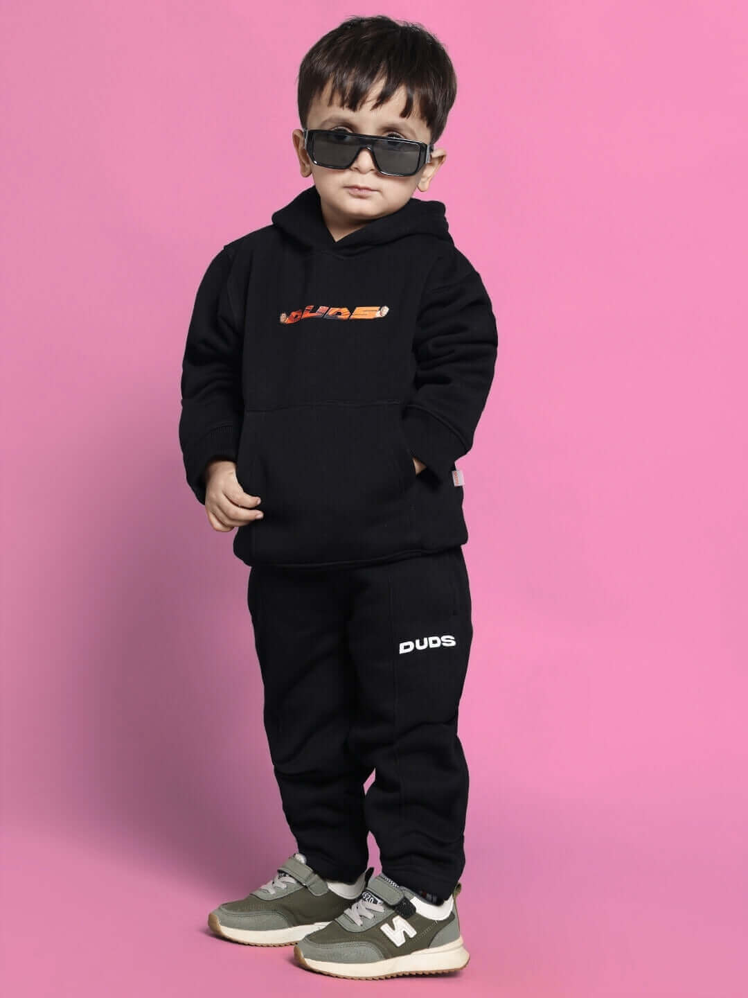 Child wearing black Gohan co-ord outfit with sunglasses on a pink background.