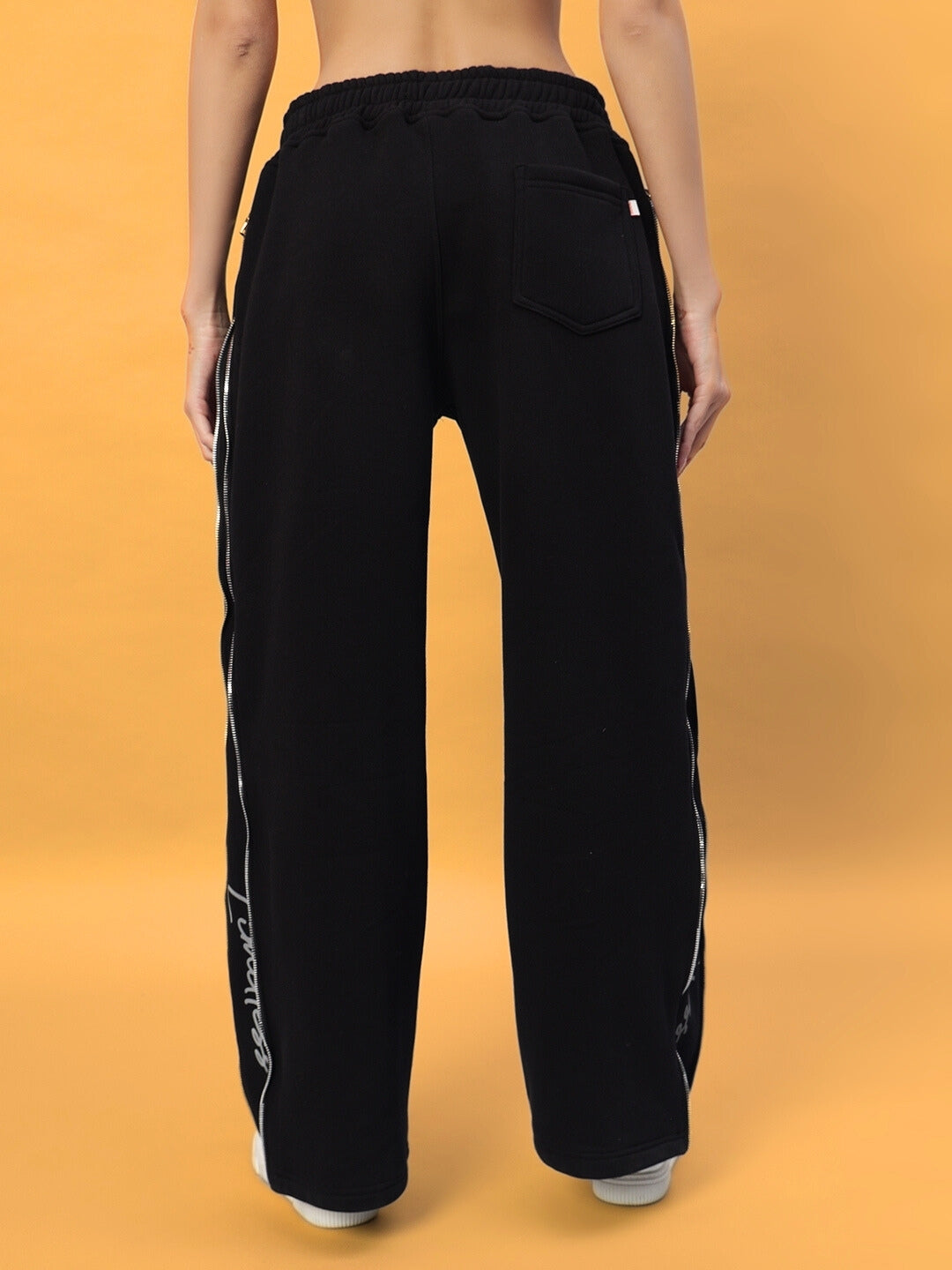Back view of Women's Limitless Fleece Reflector Jogger in black, showcasing reflector details and pocket design against a yellow backdrop.