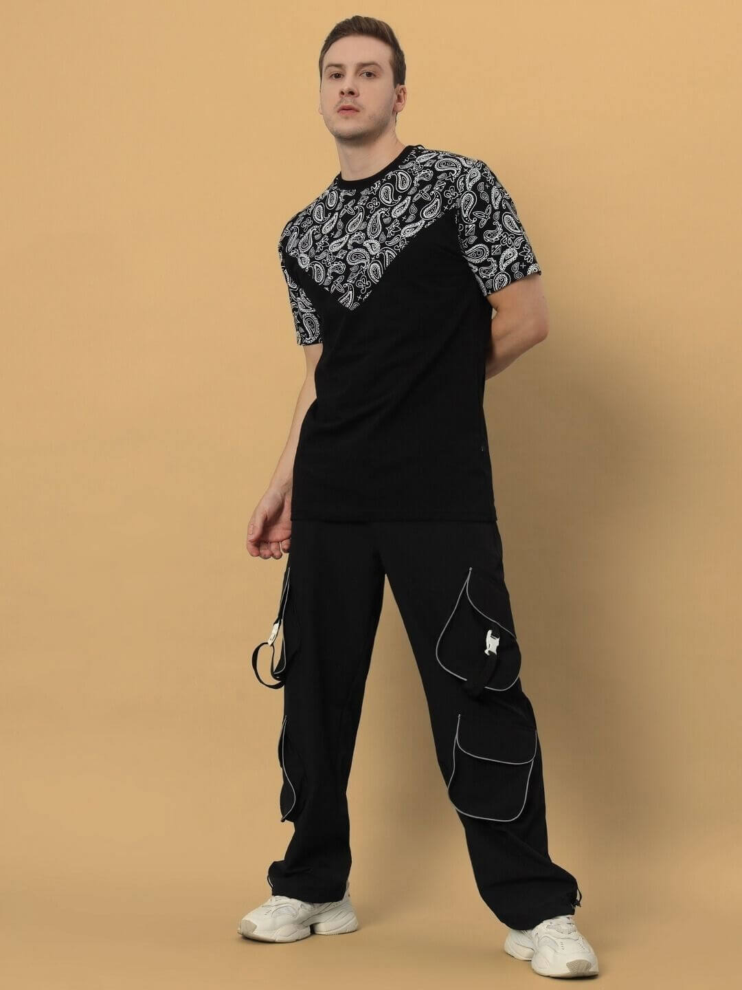 Model wearing Balladeer over-sized black t-shirt with paisley design, made from premium cotton and elastane, standing against beige background.