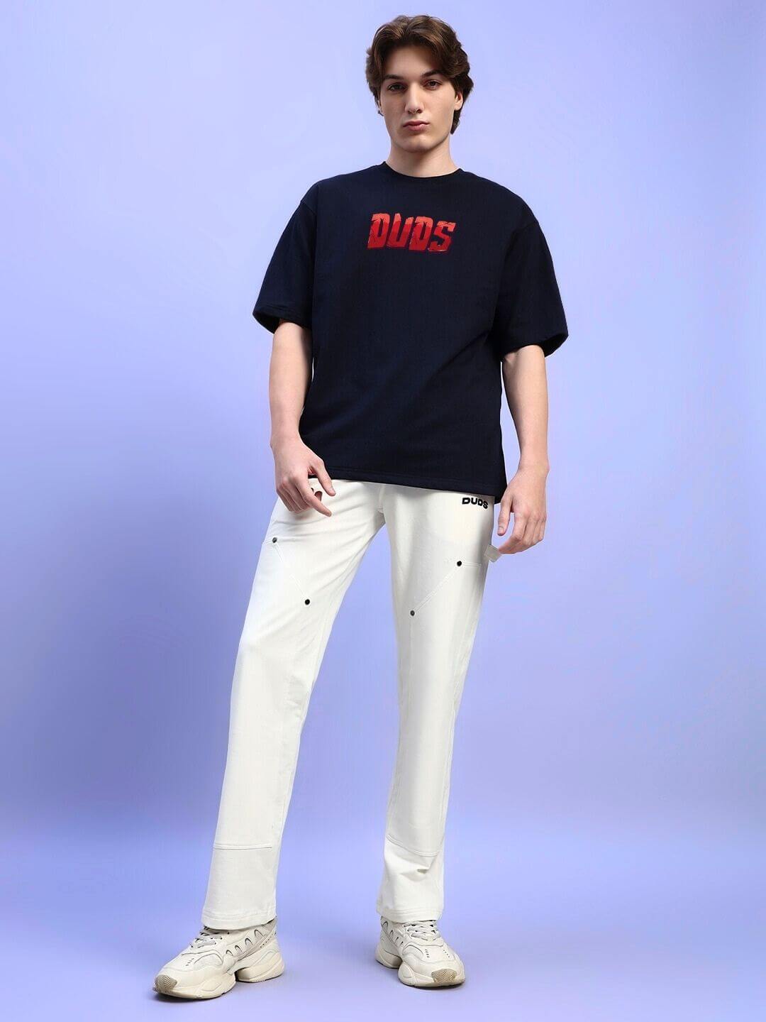 Model wearing AMPERES PRINT OVERSIZED T-SHIRT BLACK with white pants against a blue background.