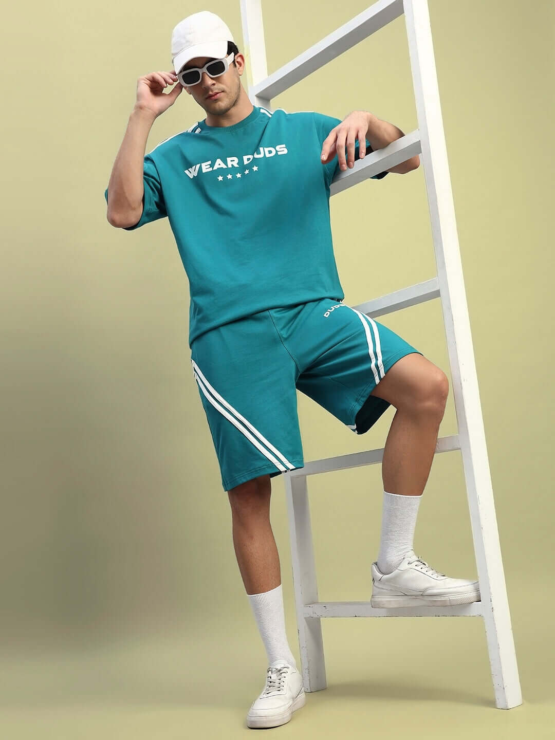 Man wearing teal STAR JUMPER Regular Fit Shorts with matching tee, leaning on a white ladder, showcasing casual sporty fashion.