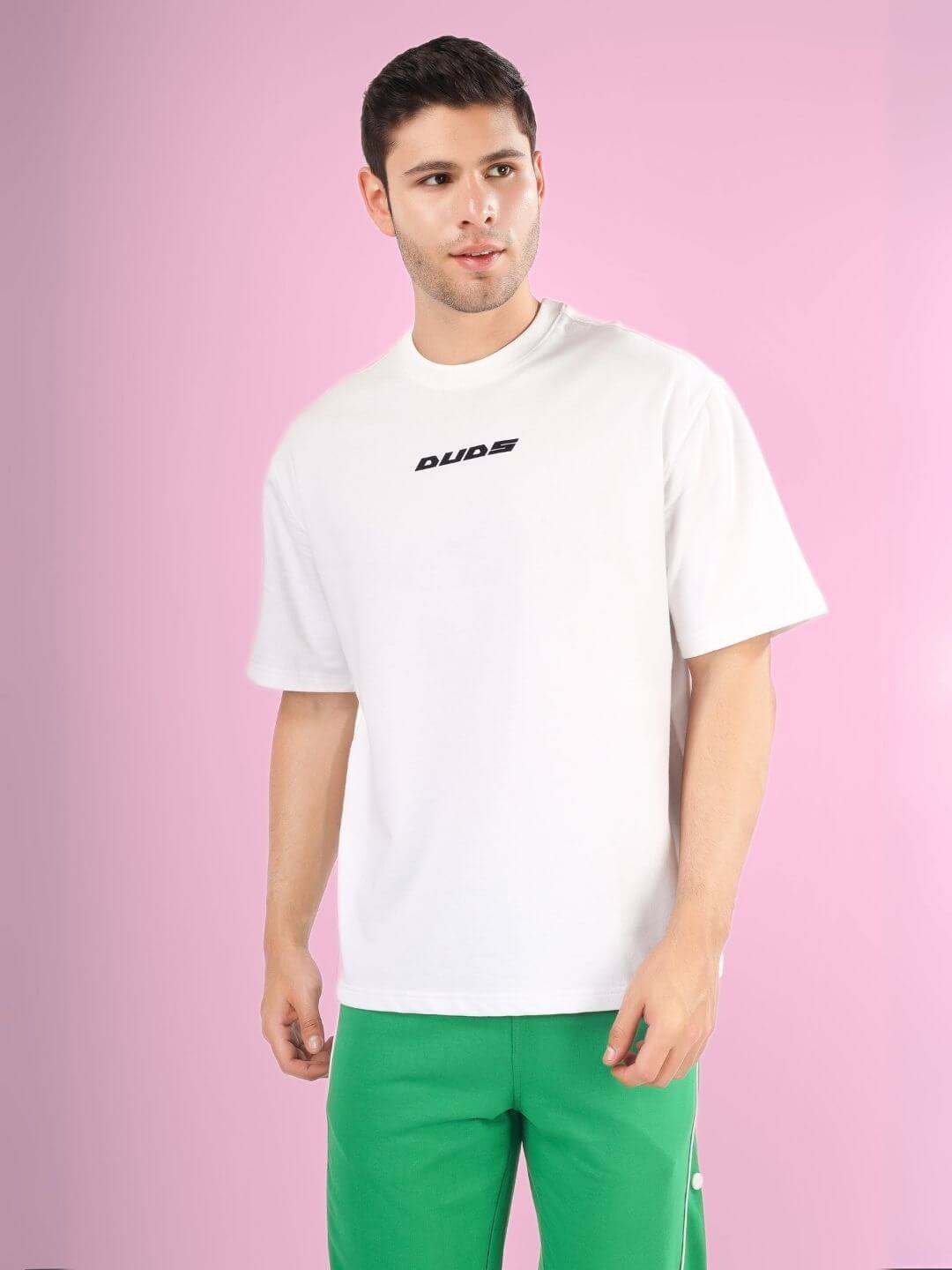 Man wearing DONT STOP OVER-SIZED T-SHIRT WHITE made of premium cotton, standing against pink background.