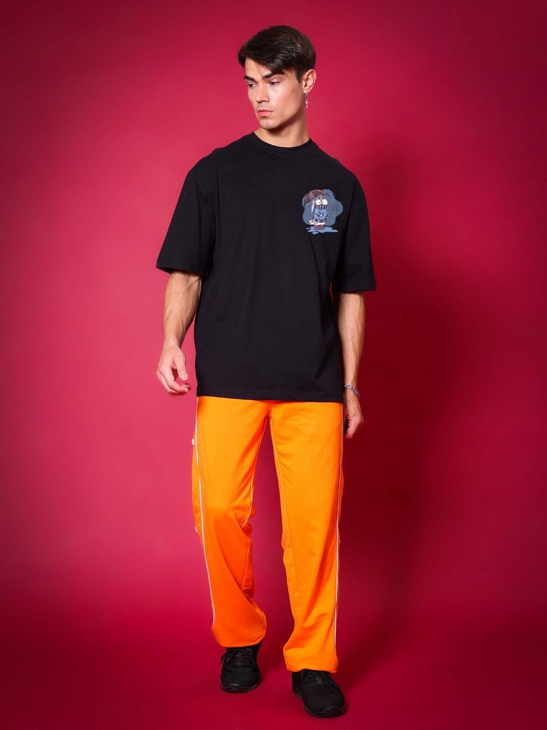 Model wearing BLUE LAPIN OVER-SIZED T-SHIRT BLACK, premium heavy gauge fabric, styled with bright orange pants on a red background.