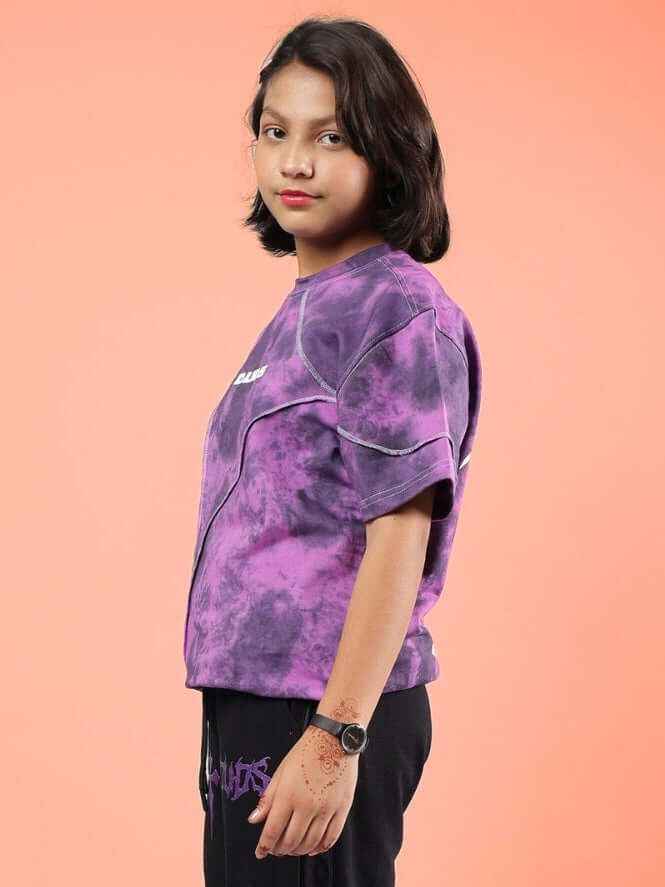 Child wearing purple ghost rider tie-dye t-shirt, side profile against peach background.