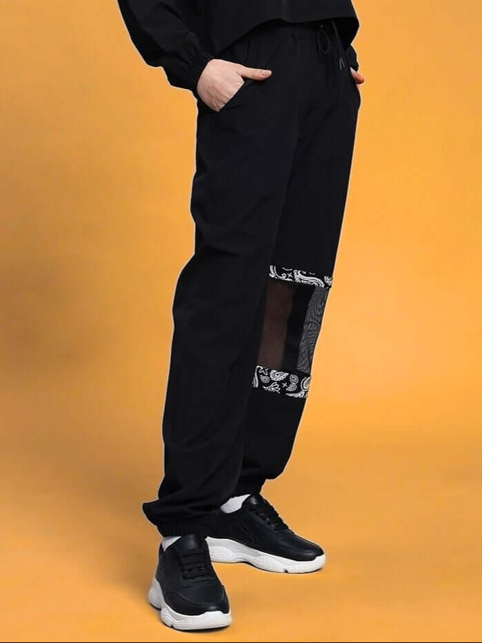 Women's Yesmin relaxed fit black cargo pant with elastic waistband, drawstring, and side pockets, styled with sneakers on orange background.