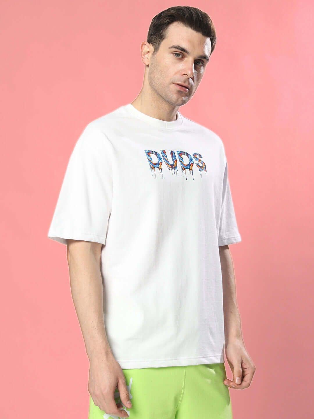 Man wearing MELTING EARTH OVER-SIZED T-SHIRT WHITE in front of a pink background, featuring bold graphic print.