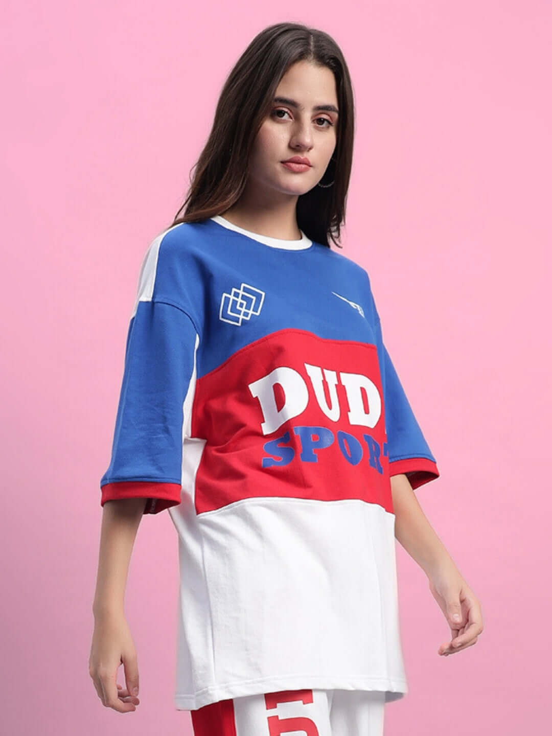 Woman wearing a multi-colored oversized urban t-shirt with bold graphics and text on a pink background.