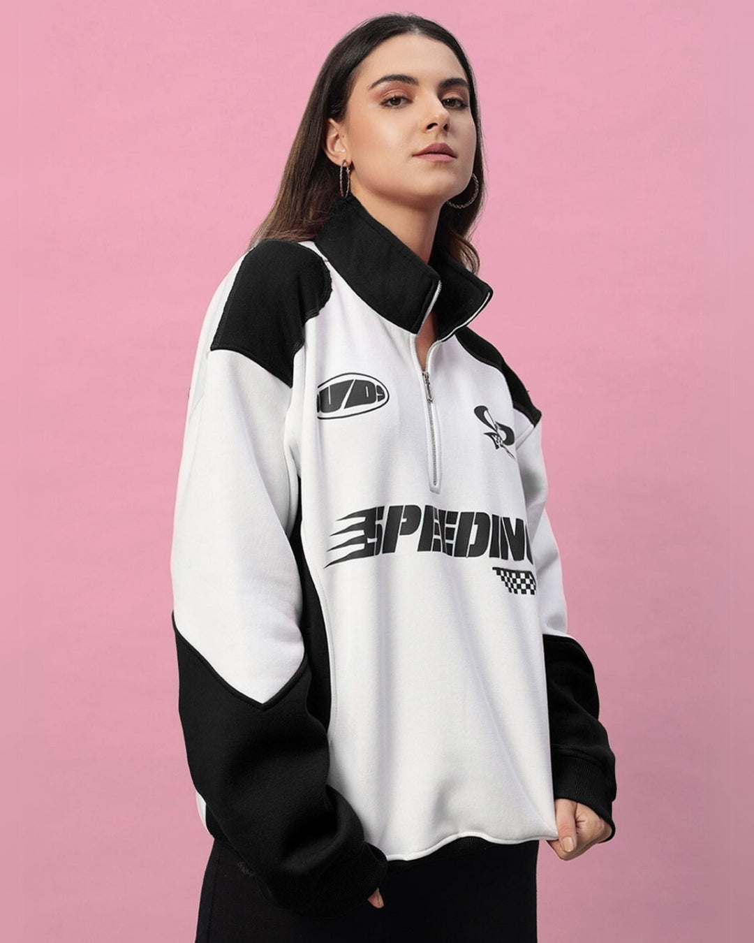 Woman wearing a black and white colorblock jacket with "Speeding" print, against a pink background.