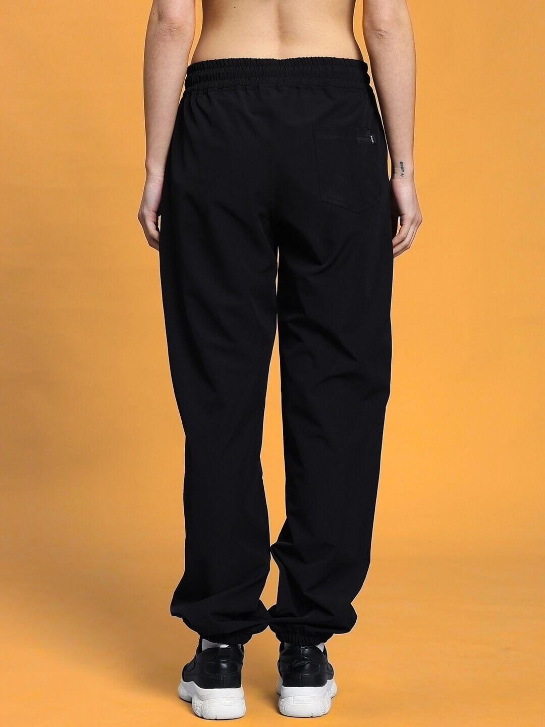 Back view of women's black relaxed fit cargo pants with elastic waistband, styled in a modern, unisex design against an orange background.